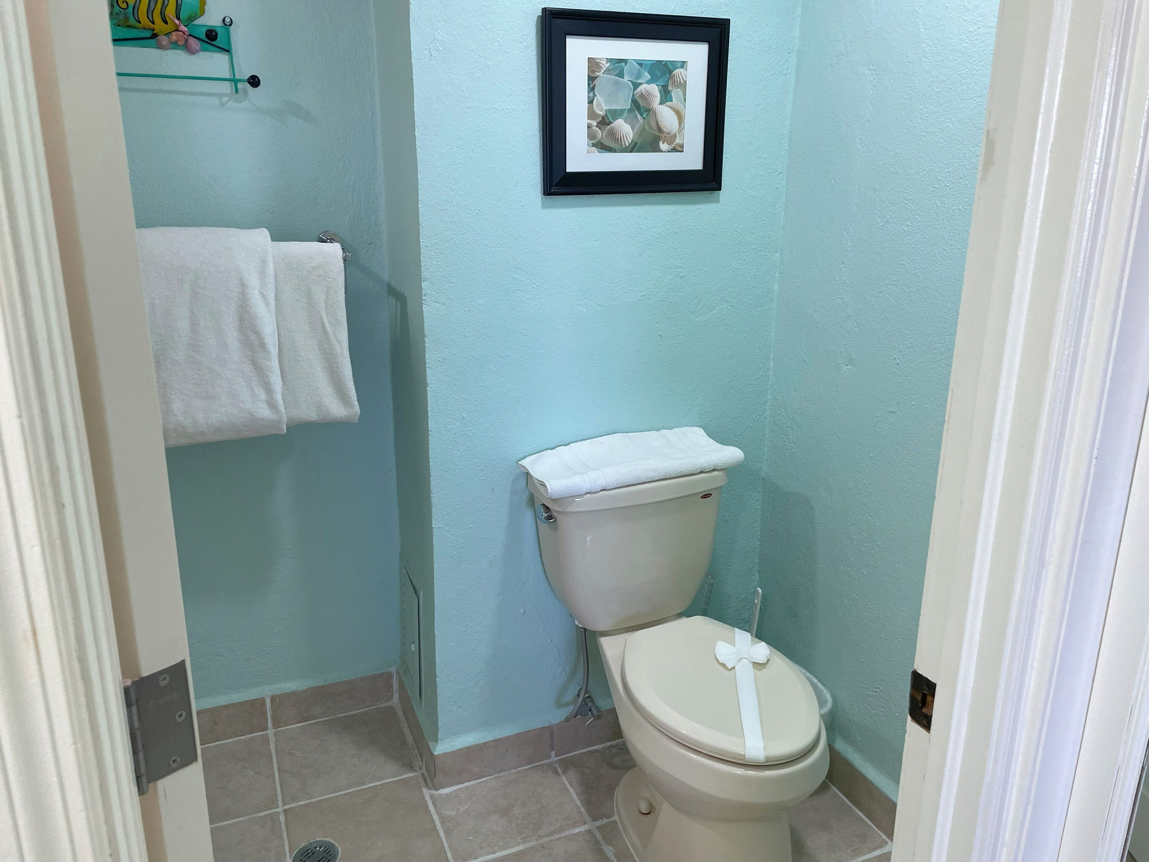 A bathroom with a toilet, a towel rack with two towels, and a framed picture on the wall.