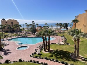 A resort pool area with a circular pool, palm trees, and a view of the ocean.