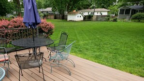 A wooden deck with metal chairs and a table, surrounded by a well-maintained lawn and a small shed.