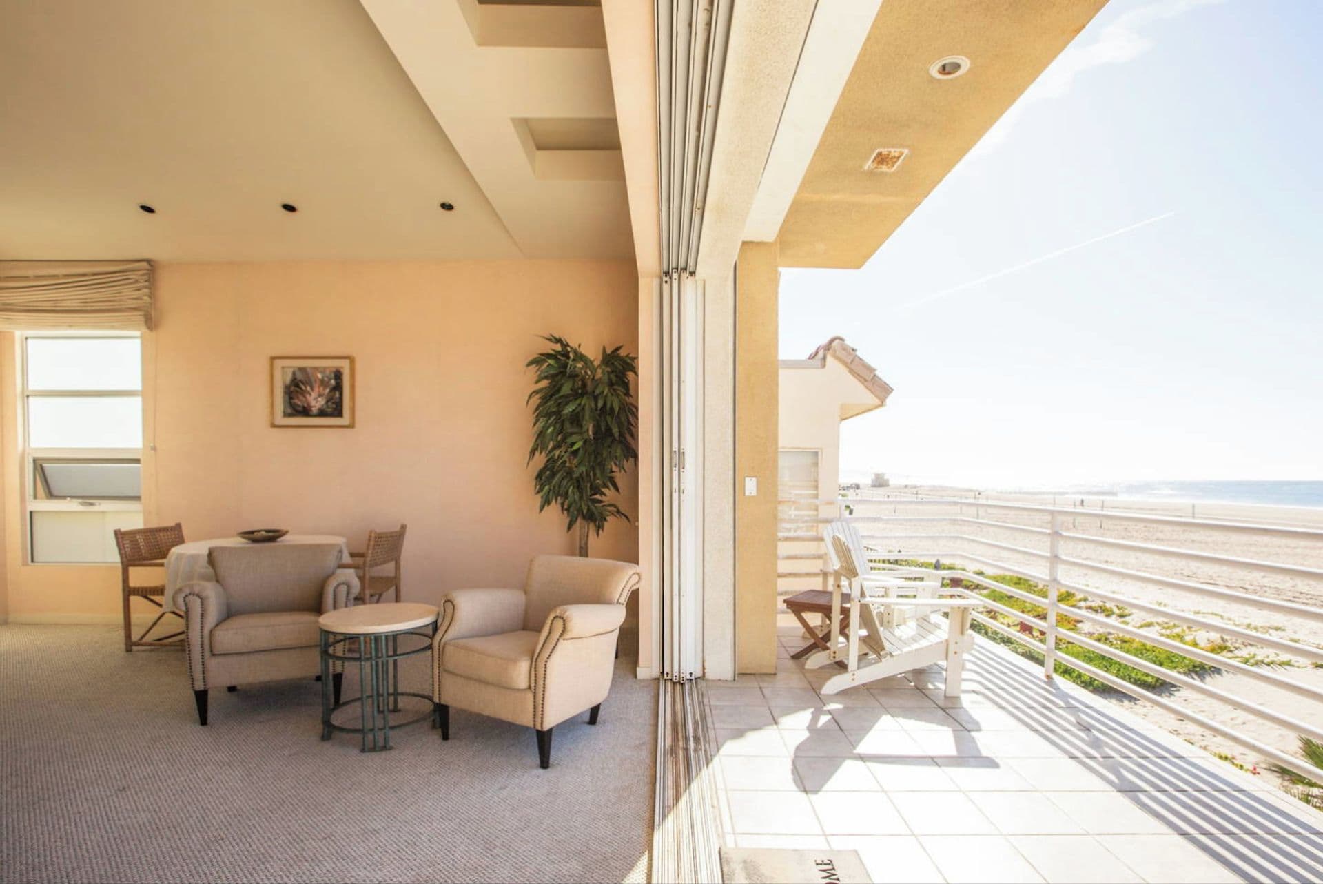 A balcony with a view of the beach, a sofa, two chairs, a small table, and a potted plant.