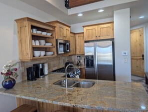Una cocina con encimeras de granito, electrodomésticos de acero inoxidable, armarios de madera y un dispensador de agua empotrado.