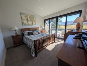 Un dormitorio con cama, escritorio, silla, lámpara, mapa en la pared y vistas al exterior.