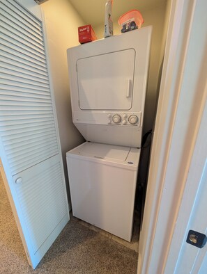 Un área de lavandería compacta con lavadora y secadora, una caja de almacenamiento y una puerta con cerradura.