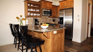 Una cocina con armarios de madera, un refrigerador de acero inoxidable, un microondas y una encimera de granito.