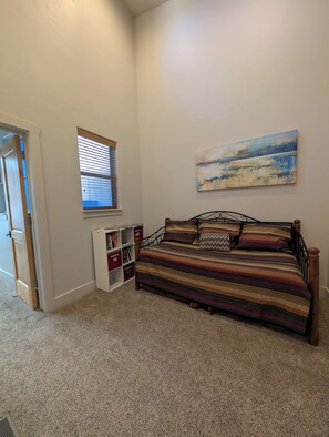 A bedroom with a bed, a window with blinds, a bookshelf, and a painting on the wall.