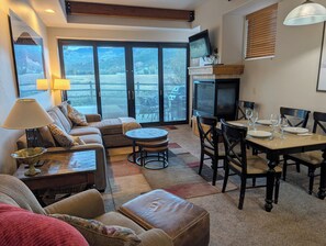 A living room with a sofa, a coffee table, a dining table set for four, and a television.