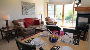 Una sala de estar con sofá, sillones, una mesa de comedor preparada para dos personas y una chimenea.