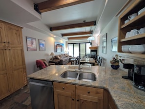 A kitchen with granite countertops, wooden cabinets, a dishwasher, and a dining area with a table and chairs.