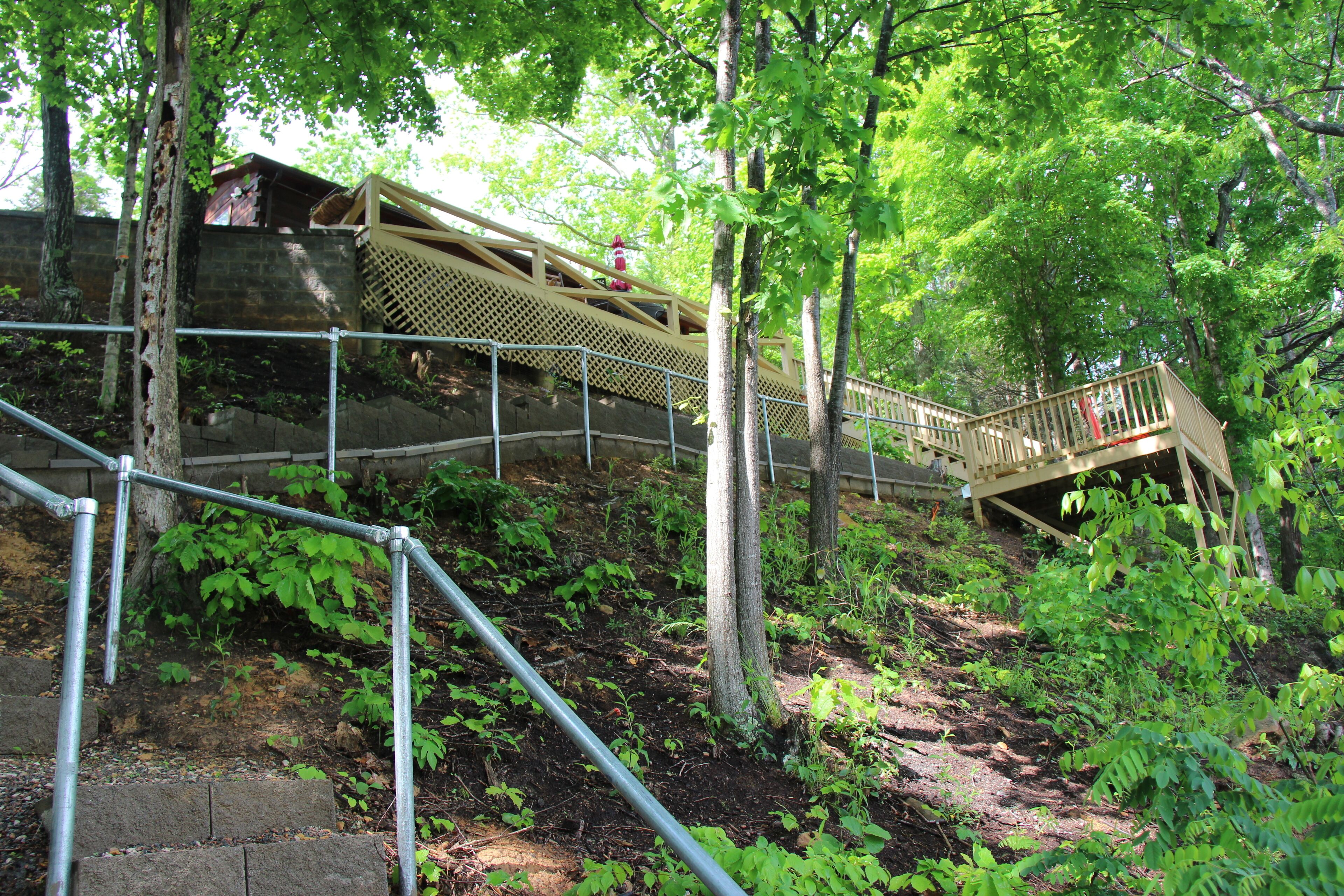 A wooden bridge with a metal railing, surrounded by trees and greenery.