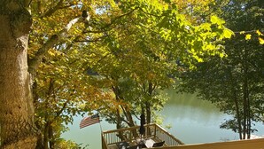 A wooden deck with a view of a lake, surrounded by trees with green and yellow leaves. - WATER FRONT CABIN FOR COUPLES! (Butler)