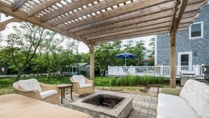 Een terras buiten met een pergola, vuurkorf en tuinmeubilair.