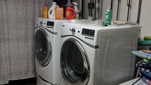 Een wasmachine met voorlader, met wasmiddelflessen en een sprayflesje erboven.