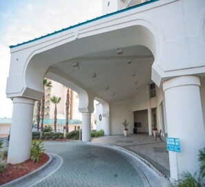 Entrada de hotel con paseo techado, palmeras y un letrero que indica acceso 'LEADING AND LEADING ONLY'.