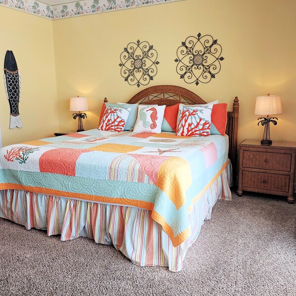 A bed with a colorful quilt, two bedside lamps, a wooden nightstand, and a decorative wall piece. - Your perfect vacation starts here in Princess 301! (Panama City Beach)