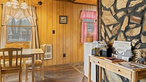 A wooden interior with a dining table and chairs, a stone wall, and a welcome sign. - Riverfront Cabin, Mountain Views, Fishing, and Rafting! (Sylva)