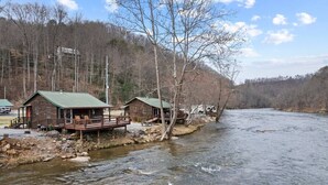 A rustic cabin-style hotel by a river with outdoor seating and a deck. - Riverfront Cabin, Mountain Views, Fishing, and Rafting! (Sylva)