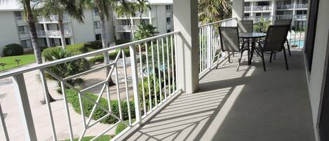 A balcony with a view of a pool and palm trees, surrounded by a white railing.