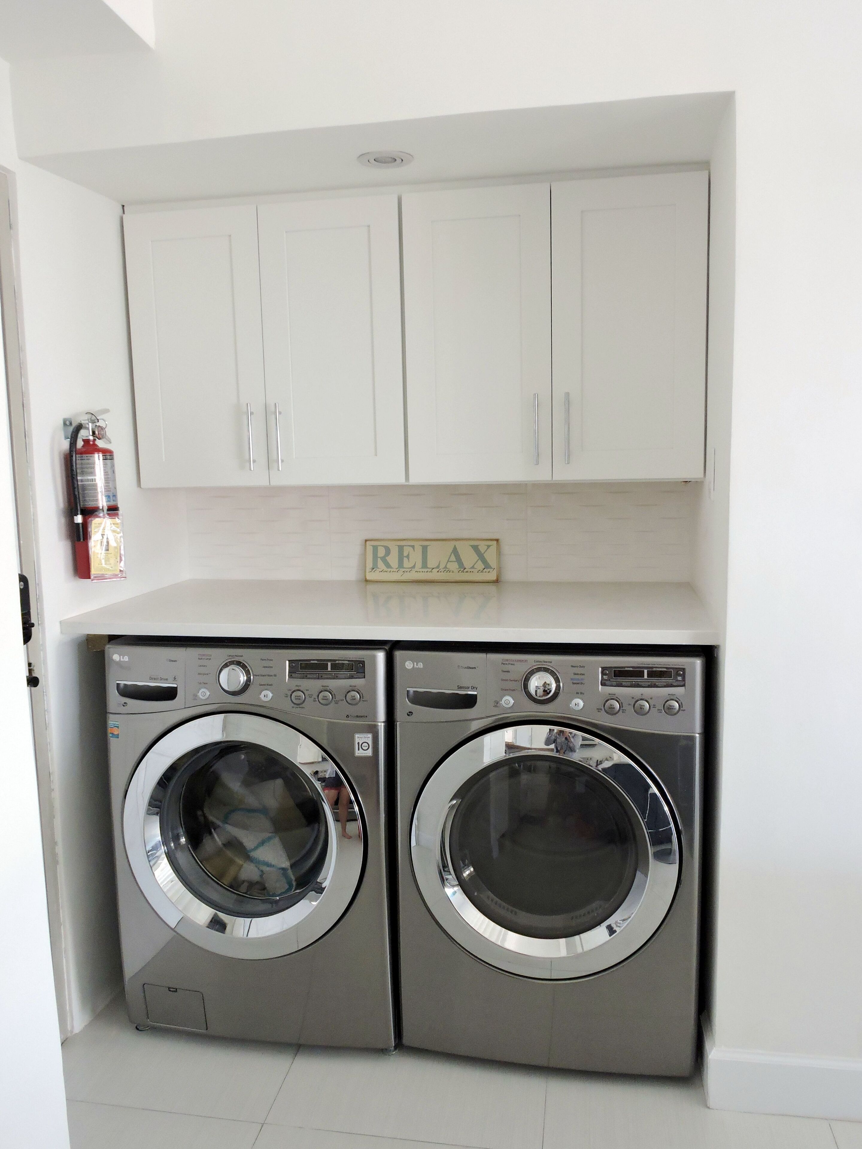 A laundry area with two front-loading washing machines, a fire extinguisher, and a 'RELAX' sign above the cabinets.