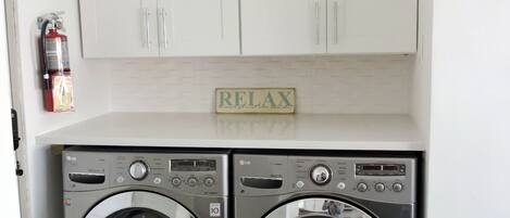 A laundry area with two front-loading washing machines, a fire extinguisher, and a 'RELAX' sign above the cabinets.