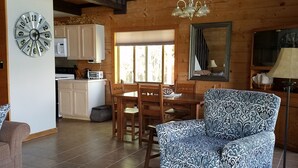 A spacious living room with a patterned armchair, a dining area with wooden furniture, and a kitchen with wooden beams and a large clock. - Time for hiking, fishing, boating  or just relaxing!  A great CO experience! (Pagosa Springs)