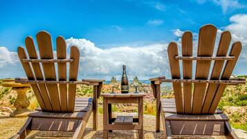 Two Adirondack chairs facing a scenic view with a bottle and glasses on a table.