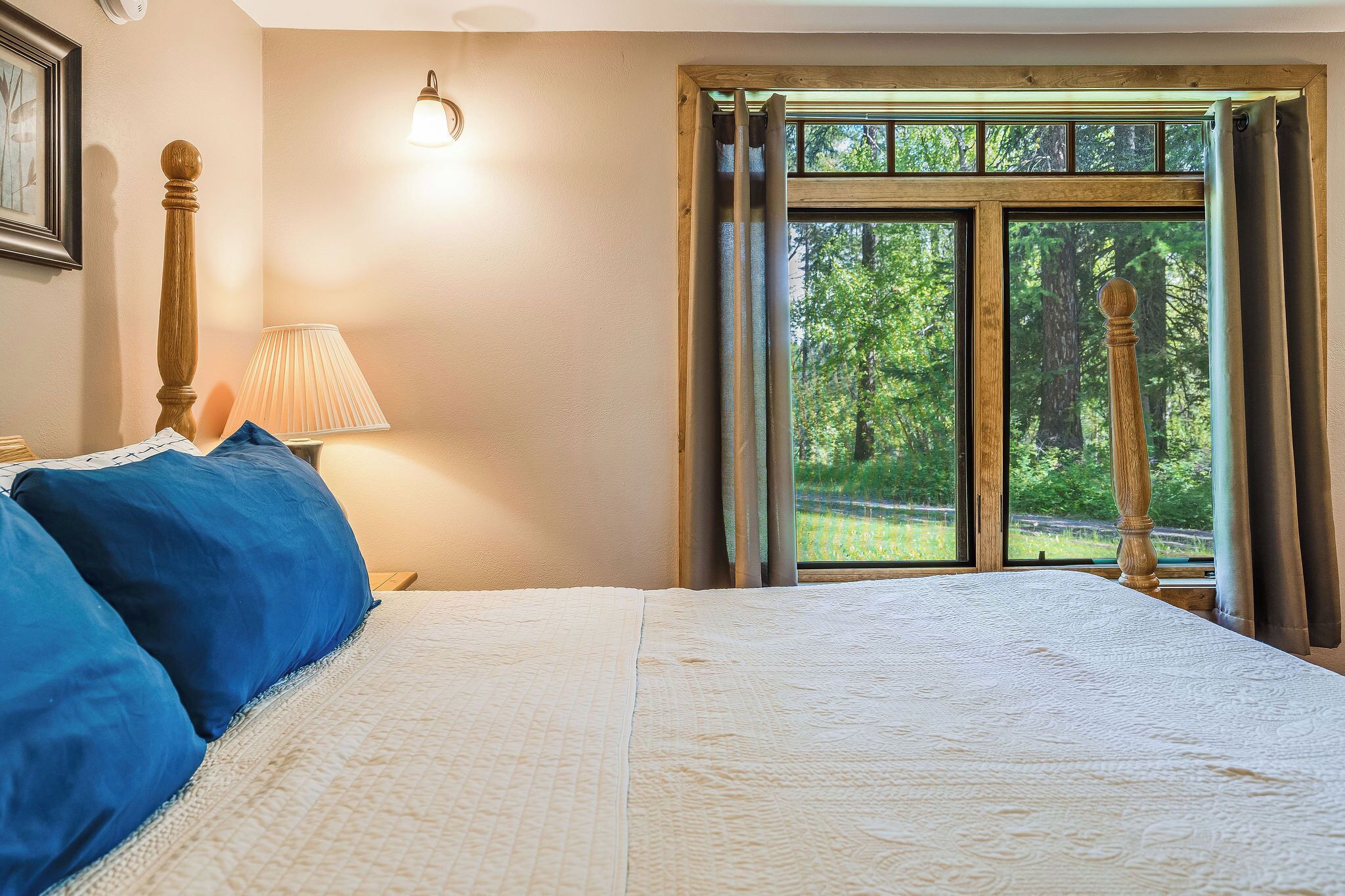 A bedroom with a large bed, a nightstand, a lamp, and a window with curtains.