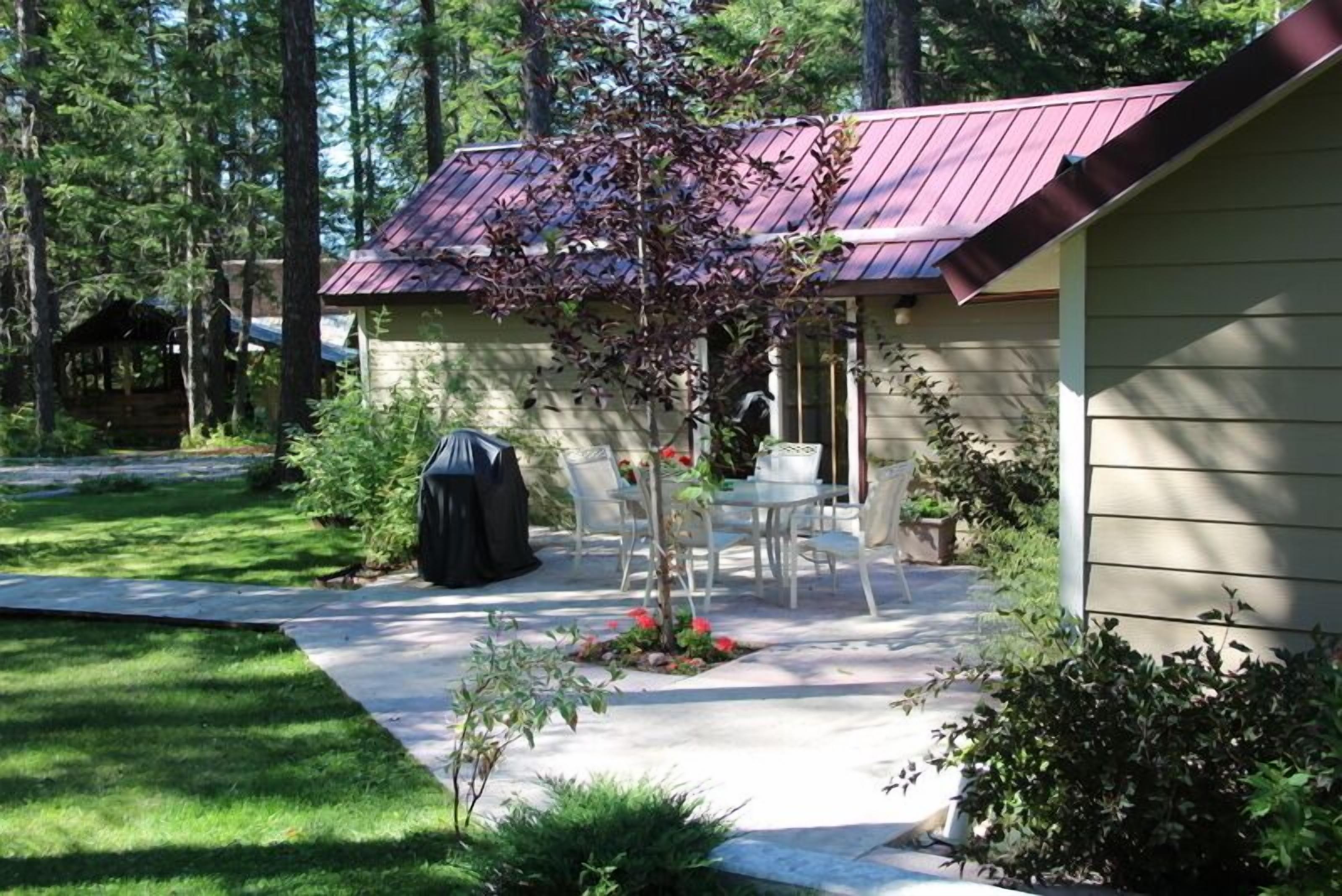 A covered patio area with a table and chairs, surrounded by greenery and a small garden.