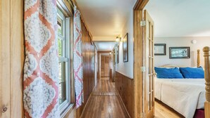 Un pasillo con pisos y paredes de madera que conduce a un dormitorio con cama y almohadas azules.