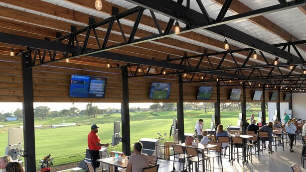 Un espacio exterior cubierto con mesas y sillas, con vista a un campo de golf.