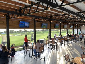 A covered outdoor seating area with tables and chairs, overlooking a golf course.