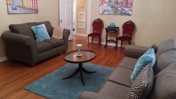 A living room with a brown sofa, a blue rug, and two armchairs. There are paintings on the walls and a small table with a vase. - CHARMING-Historic,Trinity University,Pearl Brewery, ONLY 3 miles to DT&Riverwalk (San Antonio)