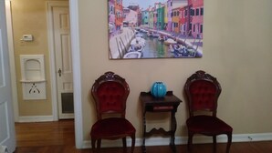 A room with two red upholstered chairs, a small table with a blue vase, and a colorful painting of a canal scene on the wall. - CHARMING-Historic,Trinity University,Pearl Brewery, ONLY 3 miles to DT&Riverwalk (San Antonio)