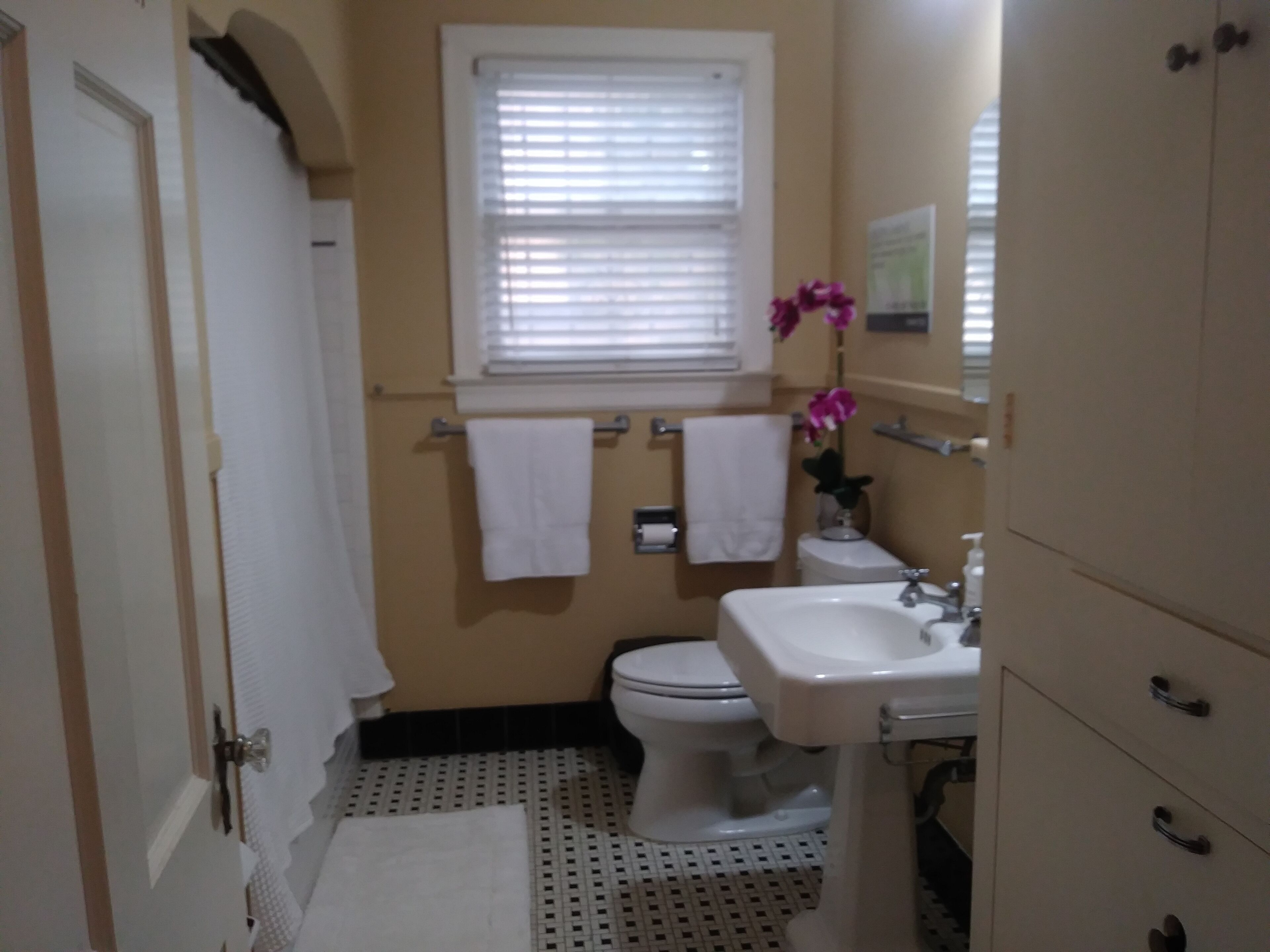 A bathroom with a toilet, sink, and window with blinds. There are two white towels hanging on the wall.