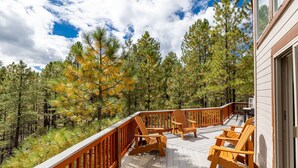 A wooden deck with Adirondack chairs, overlooking a forested area with pine trees. - Holland Home - Luxury home w/ Forest Views, AC & Hot Tub! (Flagstaff)