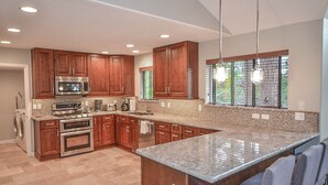 A modern kitchen with wooden cabinets, stainless steel appliances, a granite countertop, and pendant lighting. - Holland Home - Luxury home w/ Forest Views, AC & Hot Tub! (Flagstaff)
