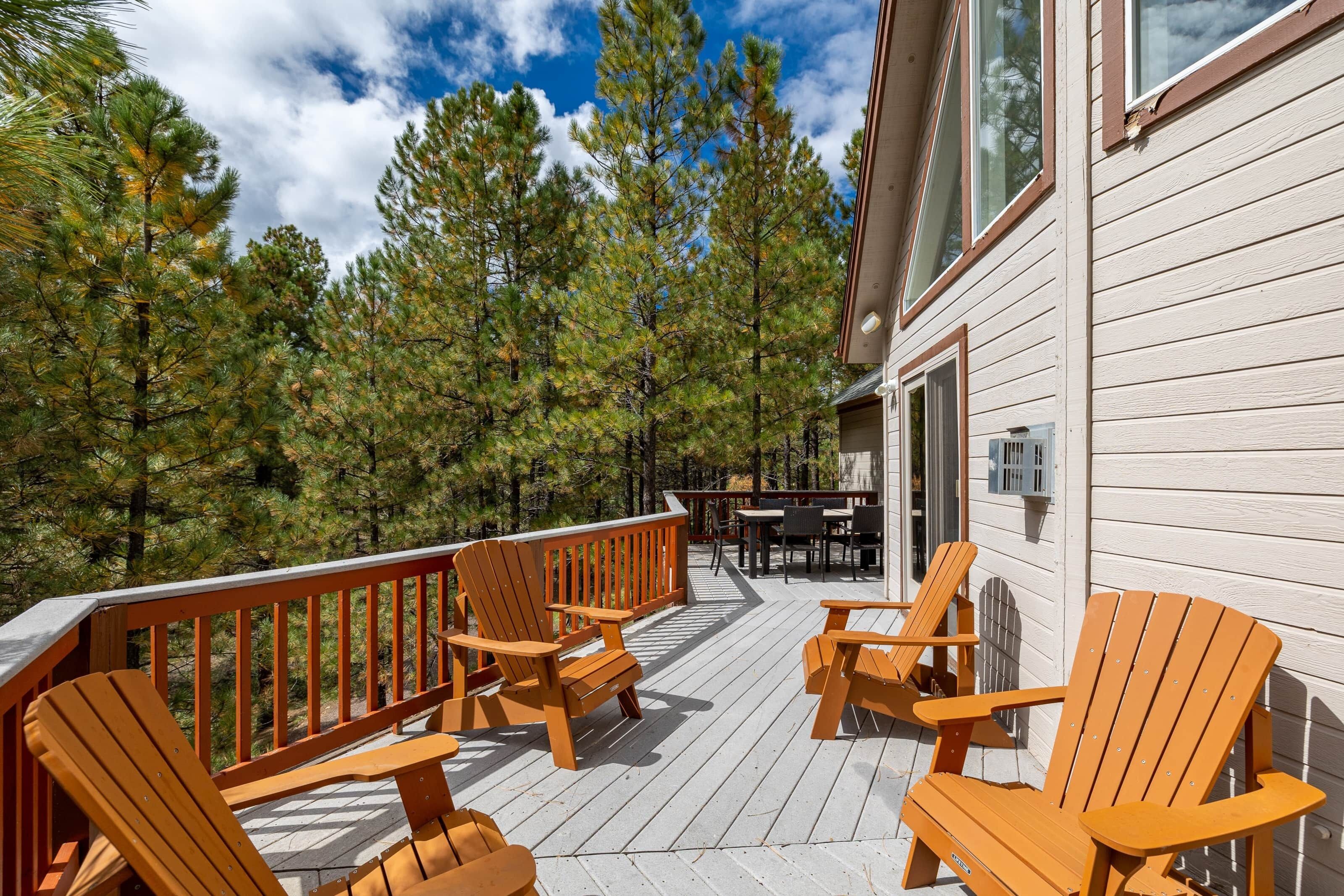 Une terrasse en bois avec des fauteuils Adirondack, une table et une vue sur une forêt.