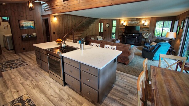 Eine geräumige Küche mit einer großen Kochinsel, Holzboden und einem gemütlichen Wohnbereich mit Sofa und Fernseher.