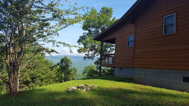 Una cabaña de madera con balcón que da a un exuberante paisaje verde y montañas lejanas.