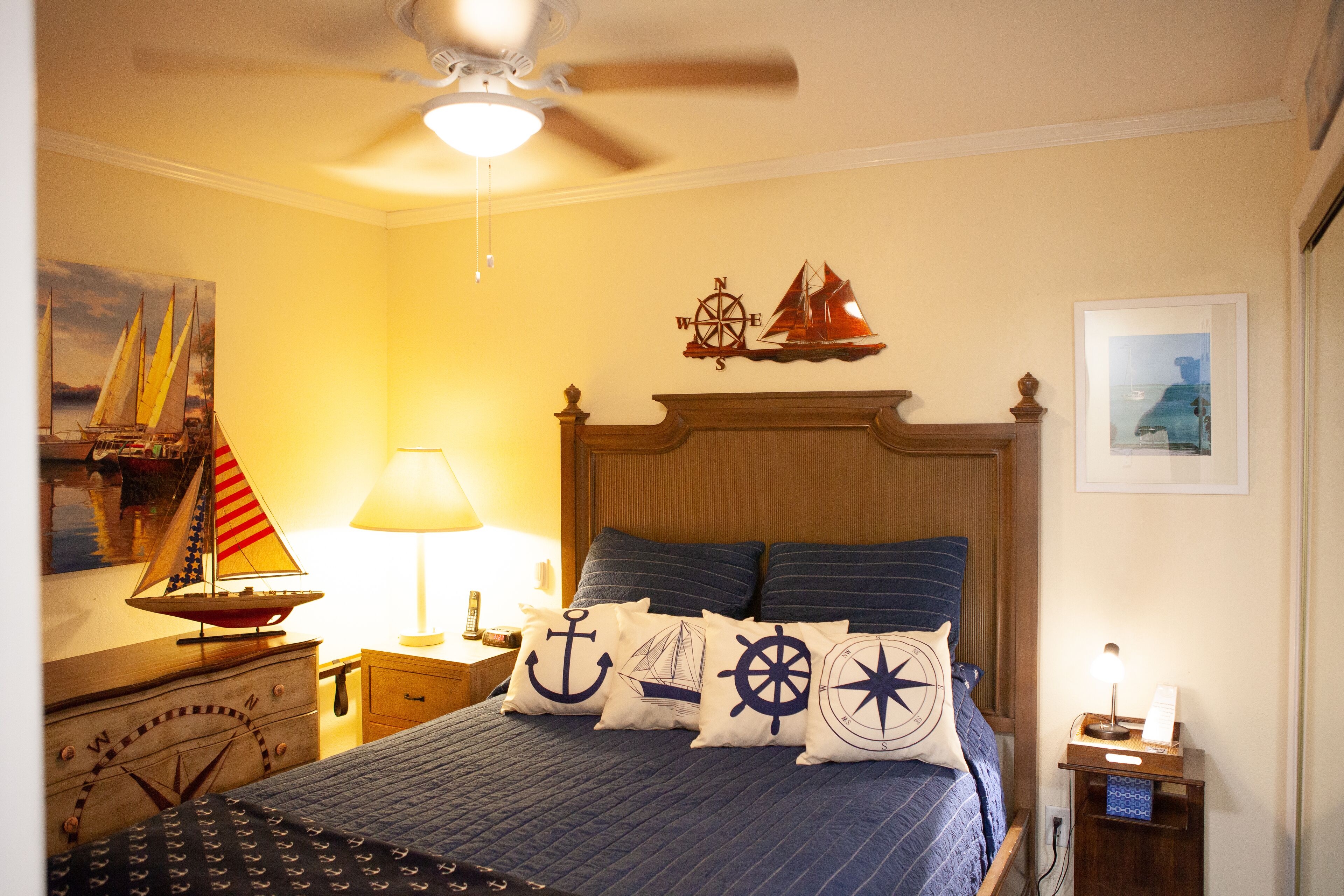 Une chambre à coucher comprenant un lit, une table de chevet, une lampe, un ventilateur de plafond et un mur décoré sur le thème de la marine.