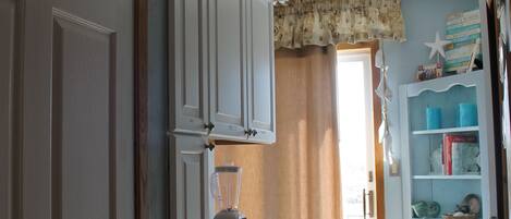 A narrow hallway with white cabinets, a door, and a window with curtains.