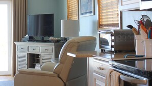 A compact kitchen with a built-in oven, a microwave, and a toaster. There is a beige armchair and a television on a small table. - Oceanfront property (Duck)