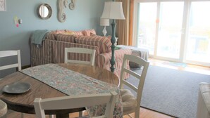 A room with a dining table, chairs, a sofa, a lamp, and a view through a sliding glass door. - Oceanfront property (Duck)