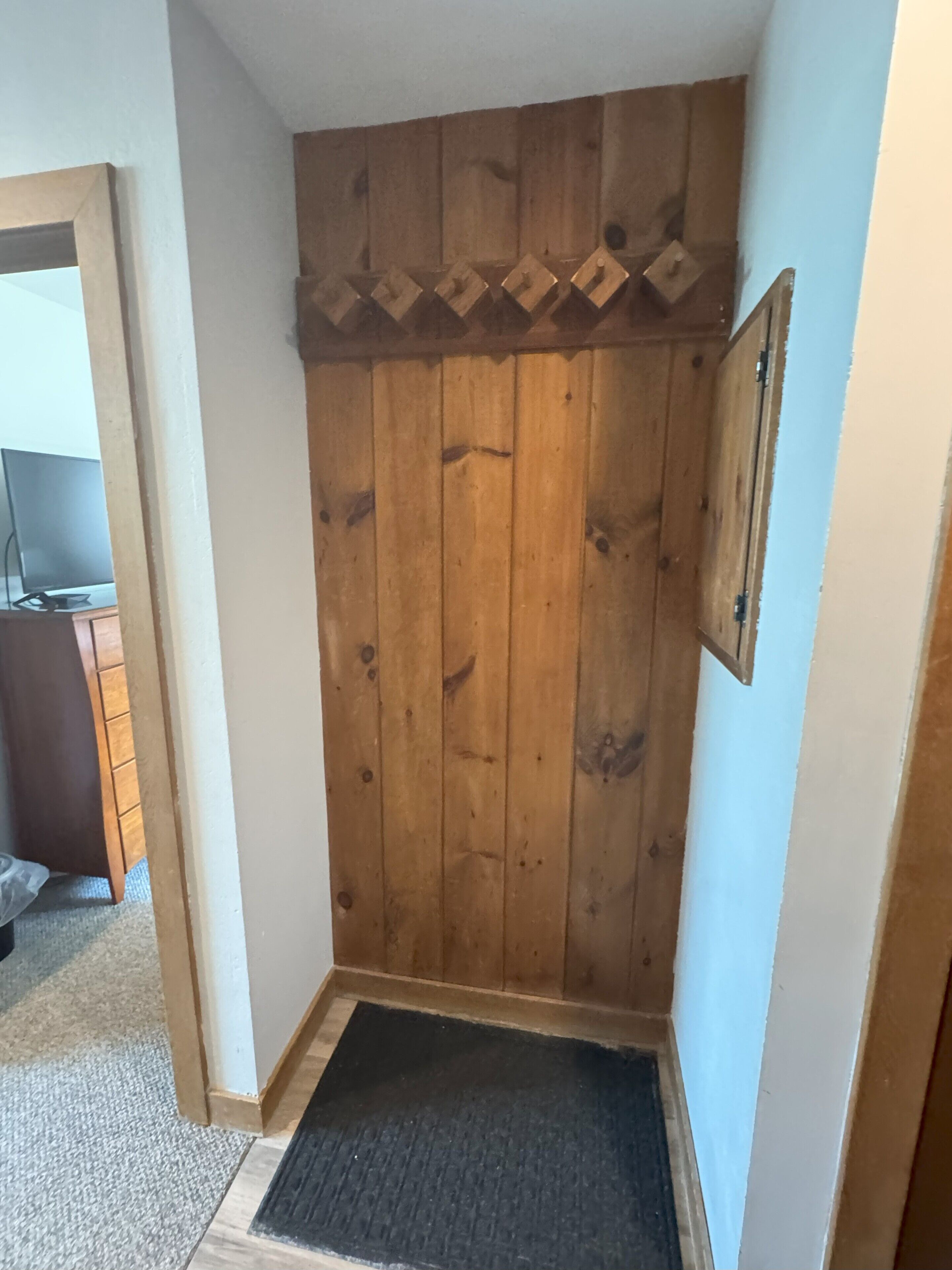 A corner room with wooden paneling, a black doormat, and a framed picture on the wall.