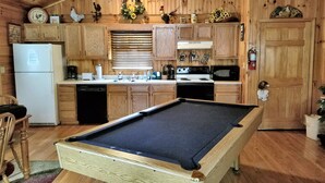 A wooden interior with a pool table, kitchen area, and wooden cabinets.