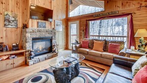 A cozy cabin interior with a stone fireplace, leather sofa, and a glass coffee table.
