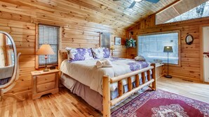 A cozy wooden cabin bedroom with a bed, bedside tables, a ceiling fan, and a large window.