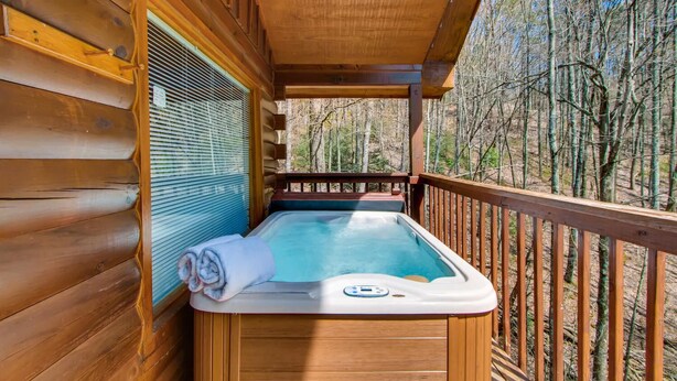 A wooden cabin with a hot tub on the deck, surrounded by trees.