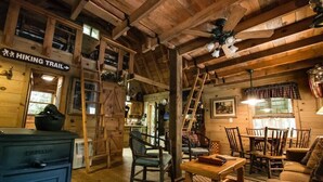 Interior rústico de una cabaña con comedor, cocina y un letrero que indica un sendero para caminatas.