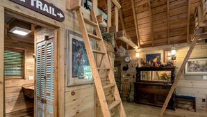 Interior rústico de una cabaña de madera con una escalera de madera, un letrero que dice "TRAIL" y un banco de madera rústico.