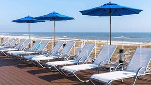Una terrazza sul mare con file di lettini e ombrelloni blu.